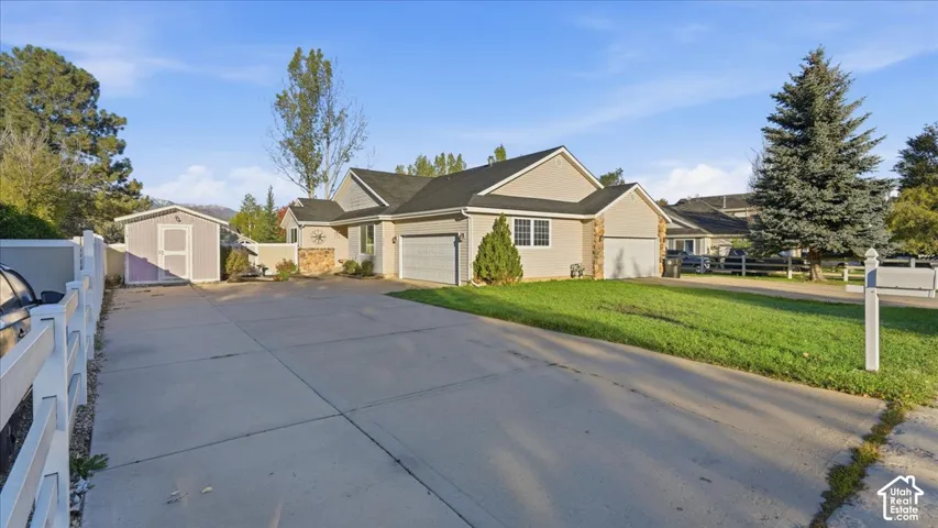 Single-story residence with a multi-car garage, stone veneer accents, neutral siding, an expansive concrete driveway, and a detached storage structure