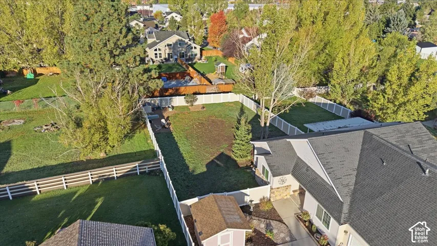 Aerial perspective of a property featuring a fenced backyard, an auxiliary storage structure, stone masonry accents, and an asphalt shingle roof
