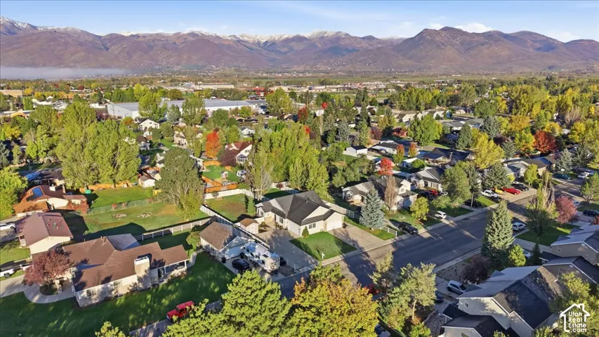 Aerial perspective showcasing the property featuring mature landscaping, a multi-car driveway, an attached garage, and prominent mountain backdrops