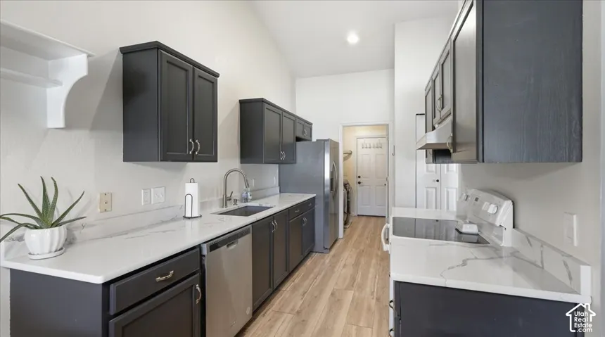 Kitchen featuring dark cabinetry, stone-finish countertops, stainless steel appliances, and wood-finish flooring