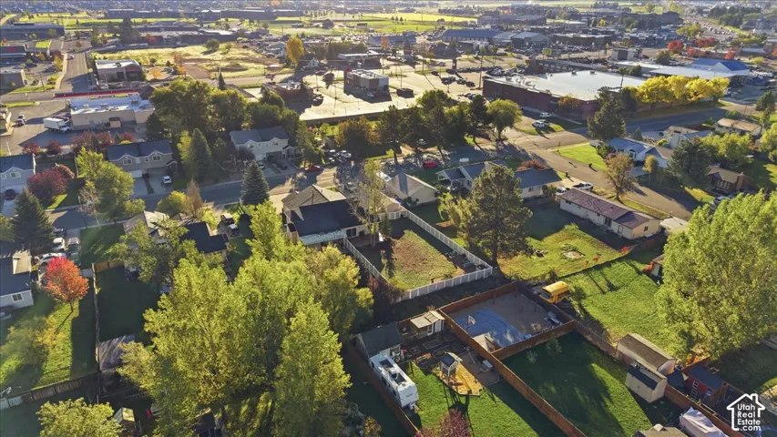 Aerial perspective featuring a residential lot with a fenced backyard, mature trees, and a multi-level roofline