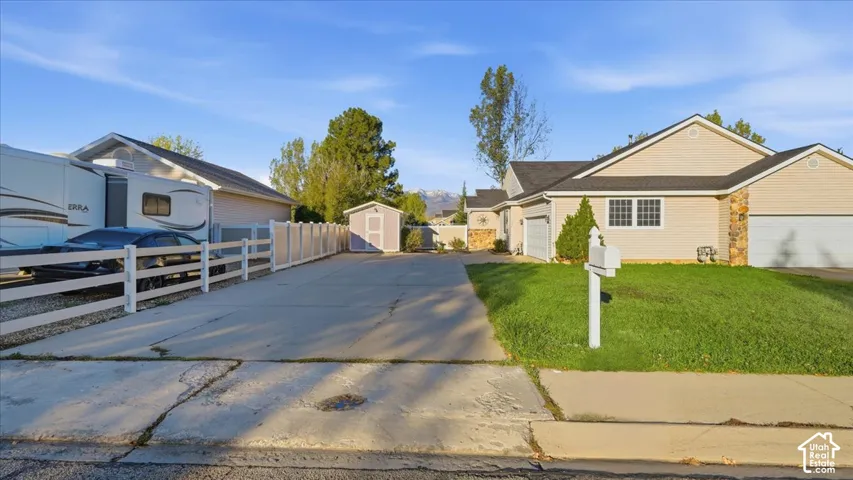 Single-story residence featuring light-colored siding, stone exterior accents, an attached multi-car garage, concrete driveway, and a detached storage shed