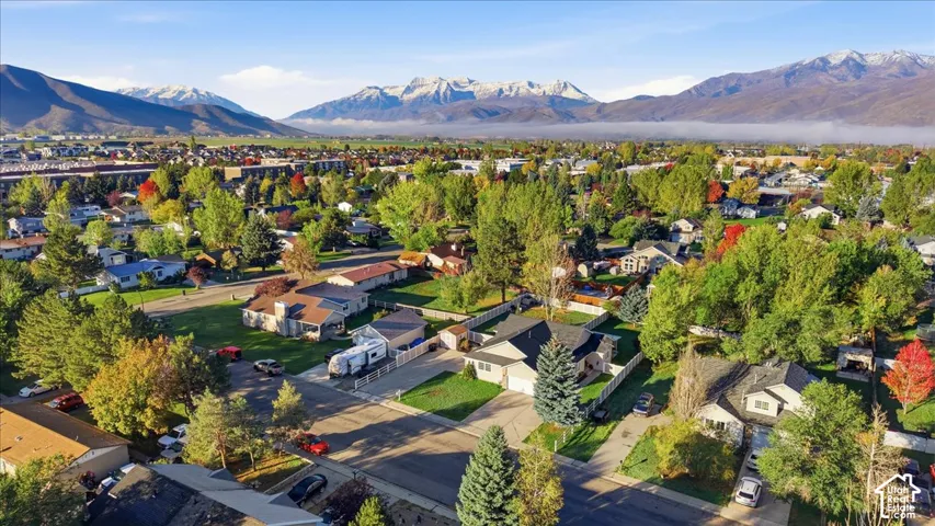 Aerial perspective of the residential property featuring a paved driveway, manicured lawn, mature trees, and an expansive mountain range backdrop