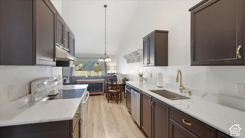 Kitchen featuring dark cabinetry, stone-surface countertops, wood-finish flooring, vaulted ceilings, and a stainless steel undermount sink with a brass-finish faucet