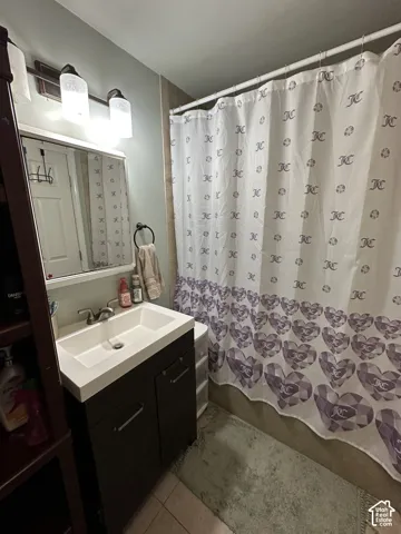 Bathroom featuring a dark-finish vanity with a rectangular integrated sink, three-light wall-mounted fixture with cylindrical shades, and tile surround shower enclosure