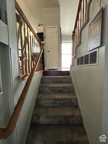 Staircase featuring wood railings with decorative balusters, carpeted treads, and a six-panel door