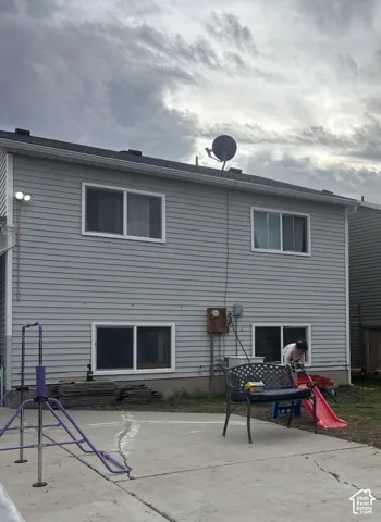 Exterior elevation featuring light-toned horizontal siding, four sliding windows, and a concrete patio