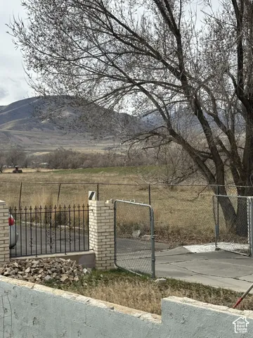 Open acreage featuring mountain terrain, chain-link and metal perimeter fencing, brick structural pillars, and concrete hardscaping