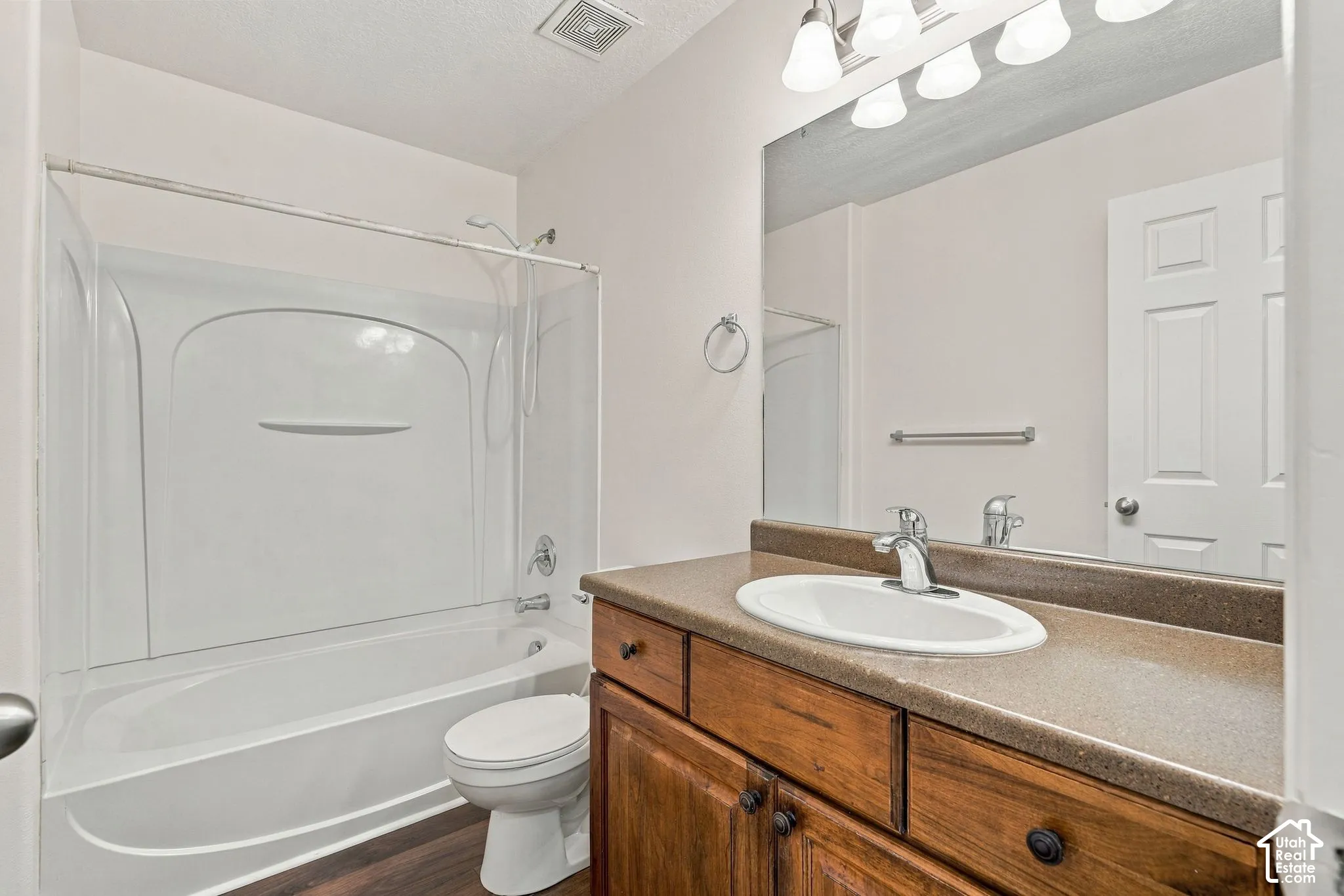 Bathroom featuring a solid-surface countertop with an integrated oval sink, wood-finish vanity cabinetry, a full-width vanity mirror, a bathtub with a white surround, and wood-finish flooring