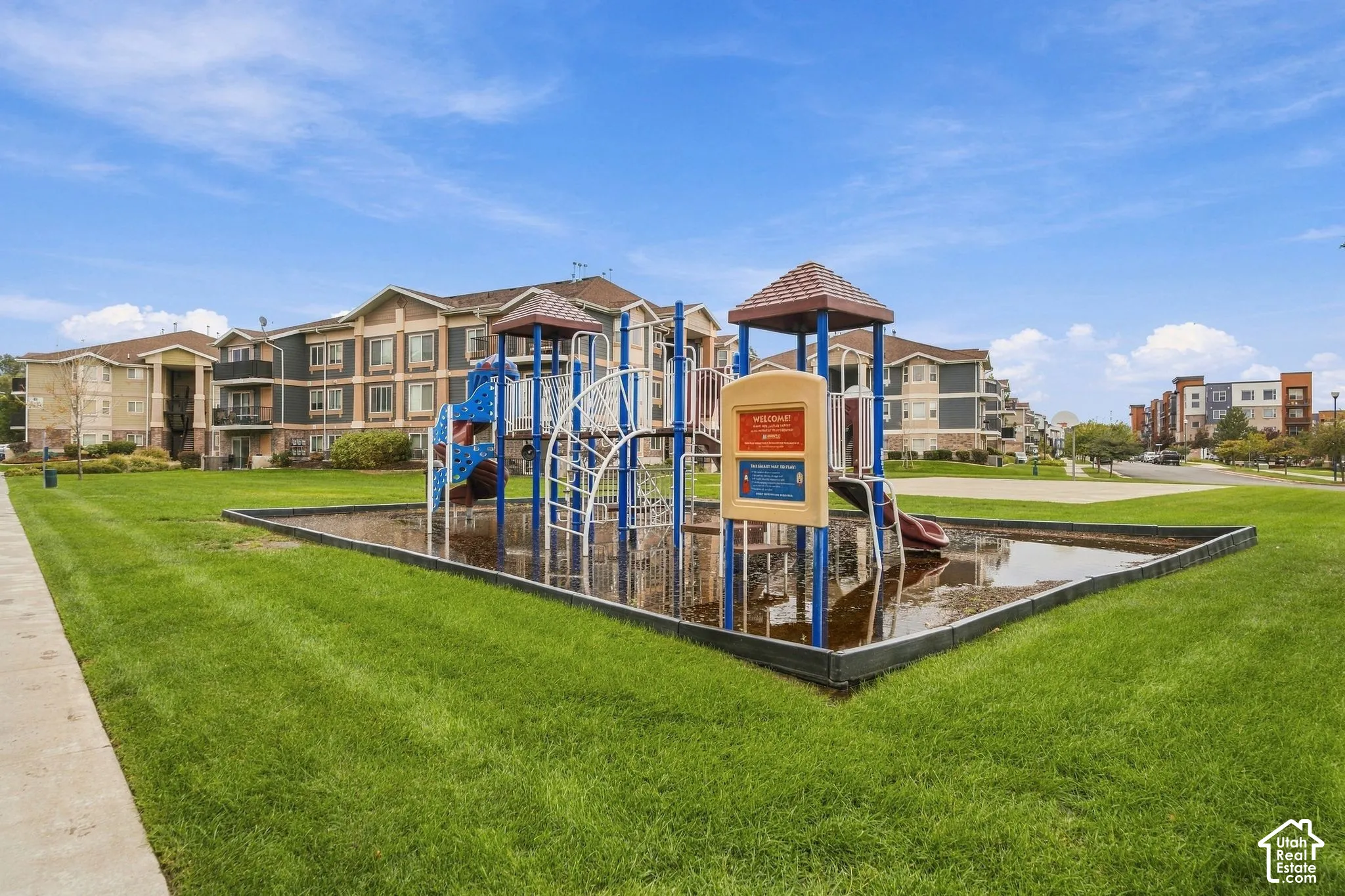 Common area featuring a playground structure, surrounding manicured lawn, and concrete walkways