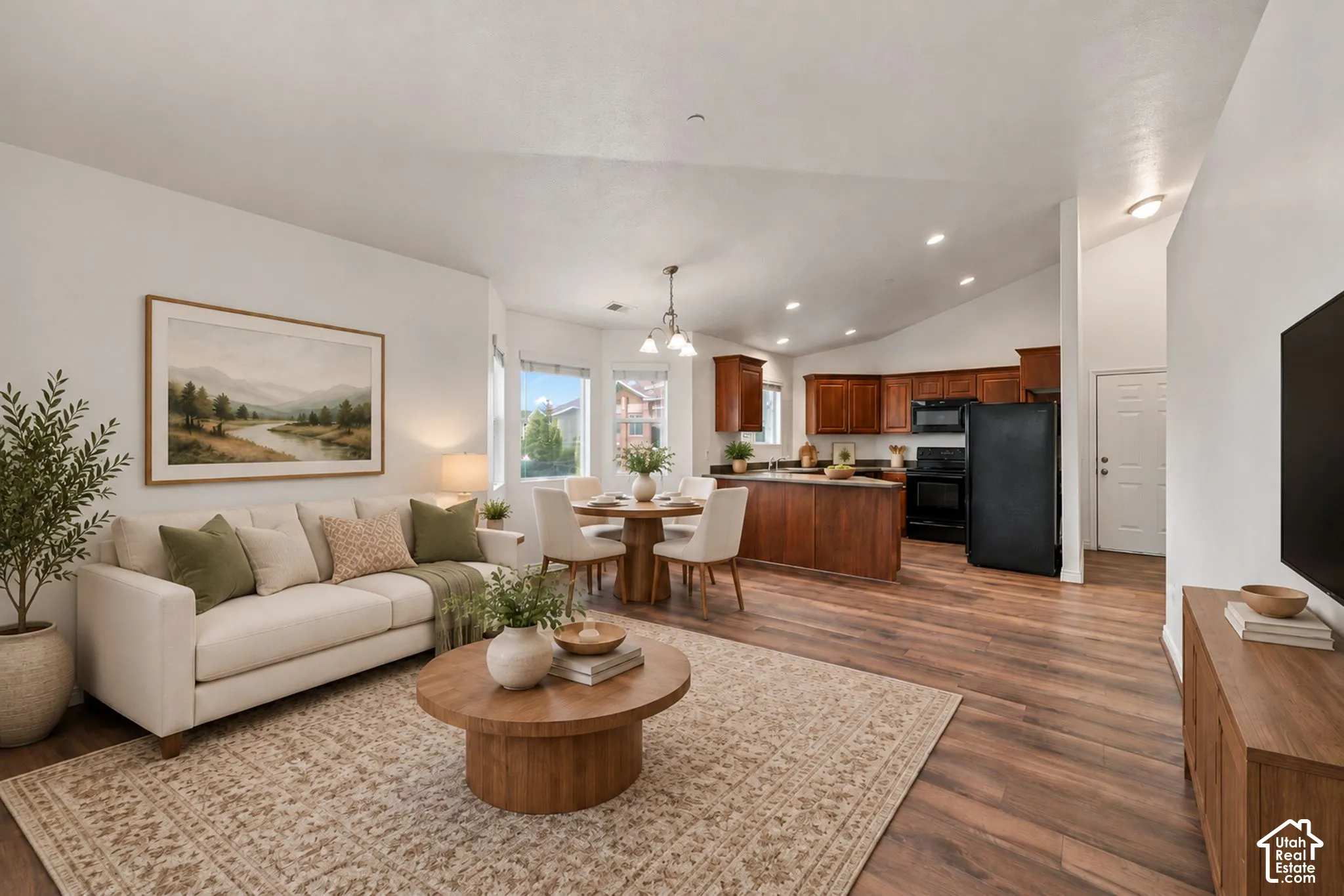Open-concept main living area featuring vaulted ceilings, recessed lighting, wood-finish flooring, and cabinetry with dark-toned countertops