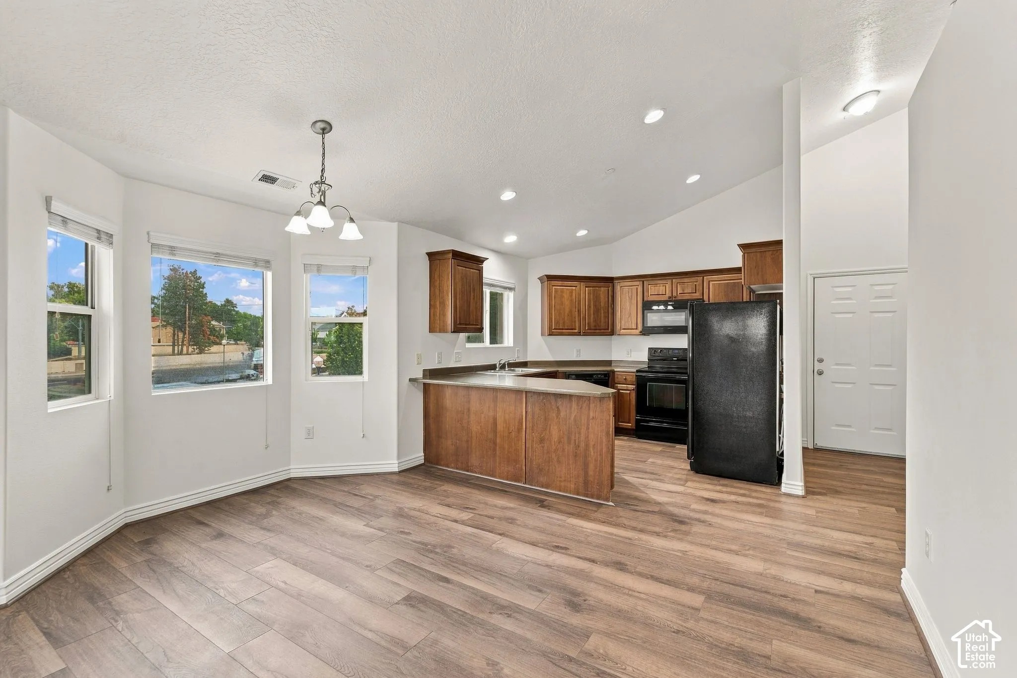 Kitchen featuring wood-finish cabinetry, a peninsula counter, recessed lighting, and wood-finish flooring, complemented by windows in a bay configuration