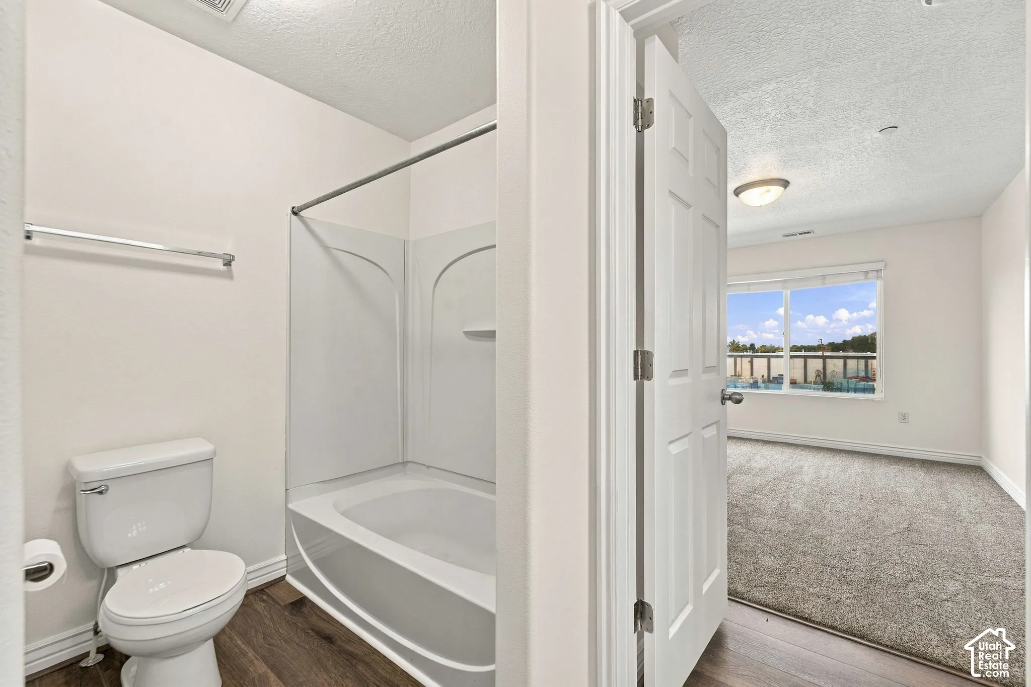 Bathroom featuring a molded composite tub and shower surround, white toilet, wall-mounted towel bar, and wood-finish flooring
