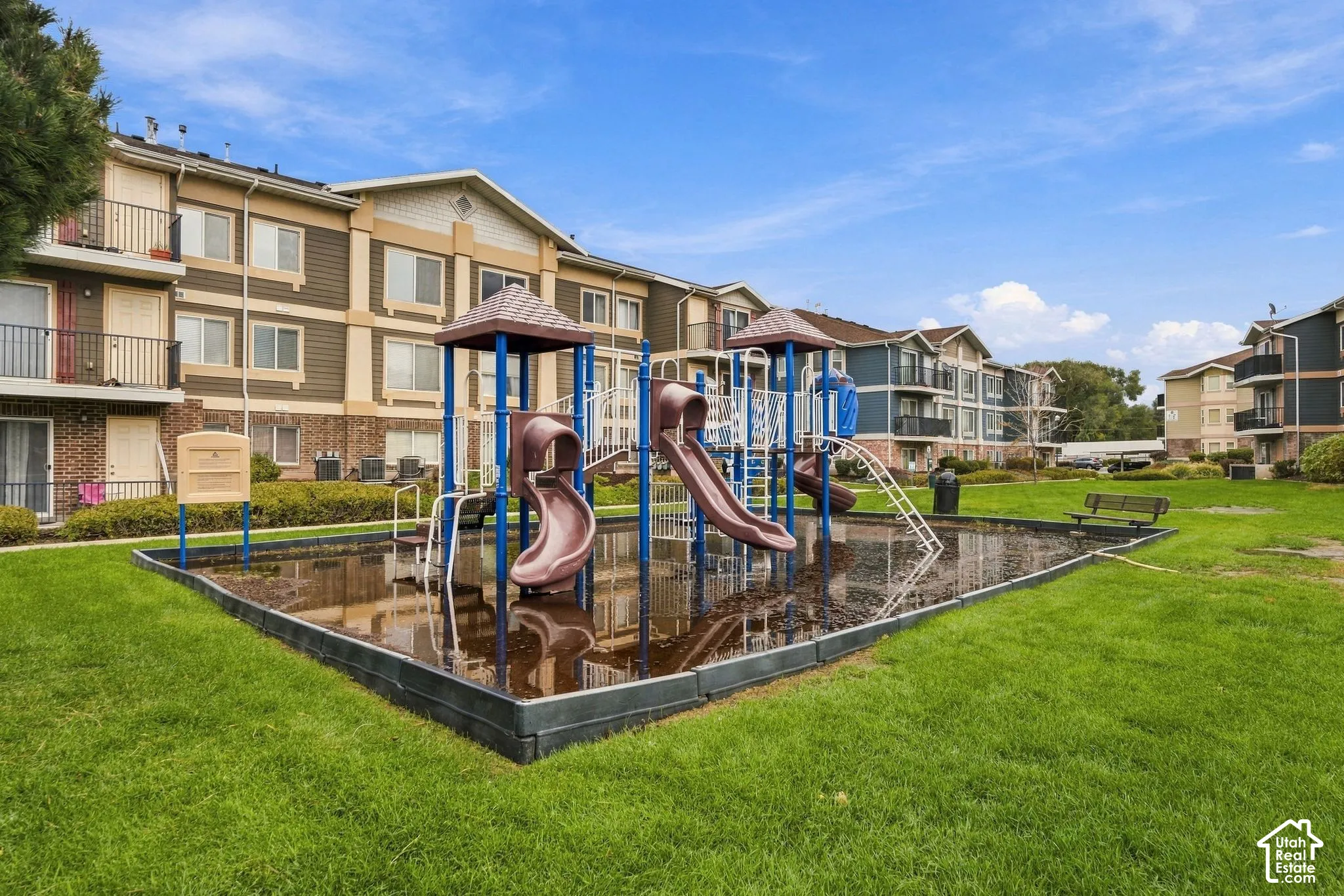 Communal recreation area featuring a playground structure with slides, integrated landscape curbing, and manicured green space