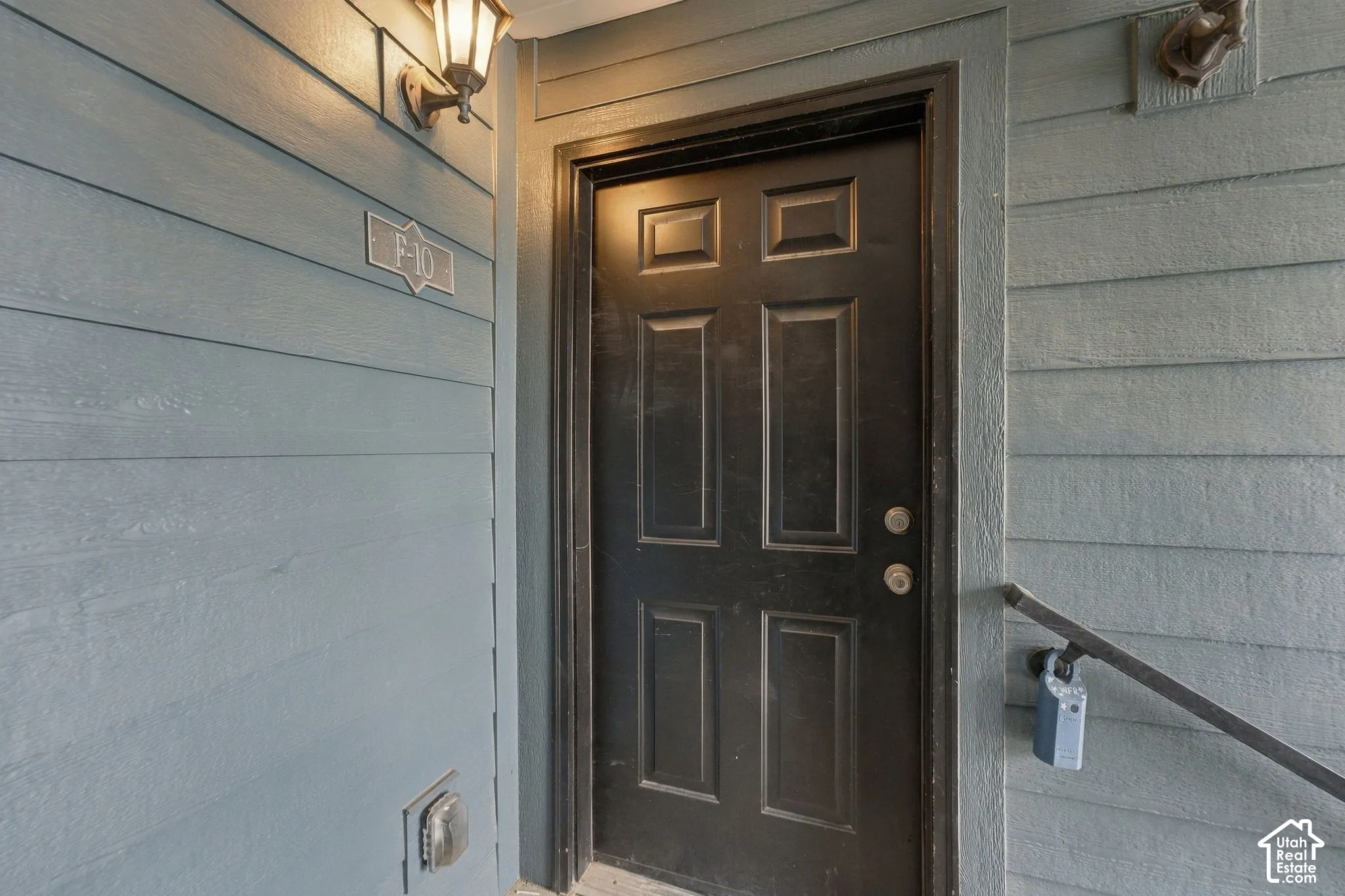 Entryway featuring horizontal siding, a solid six-panel door, and wall-mounted exterior lighting