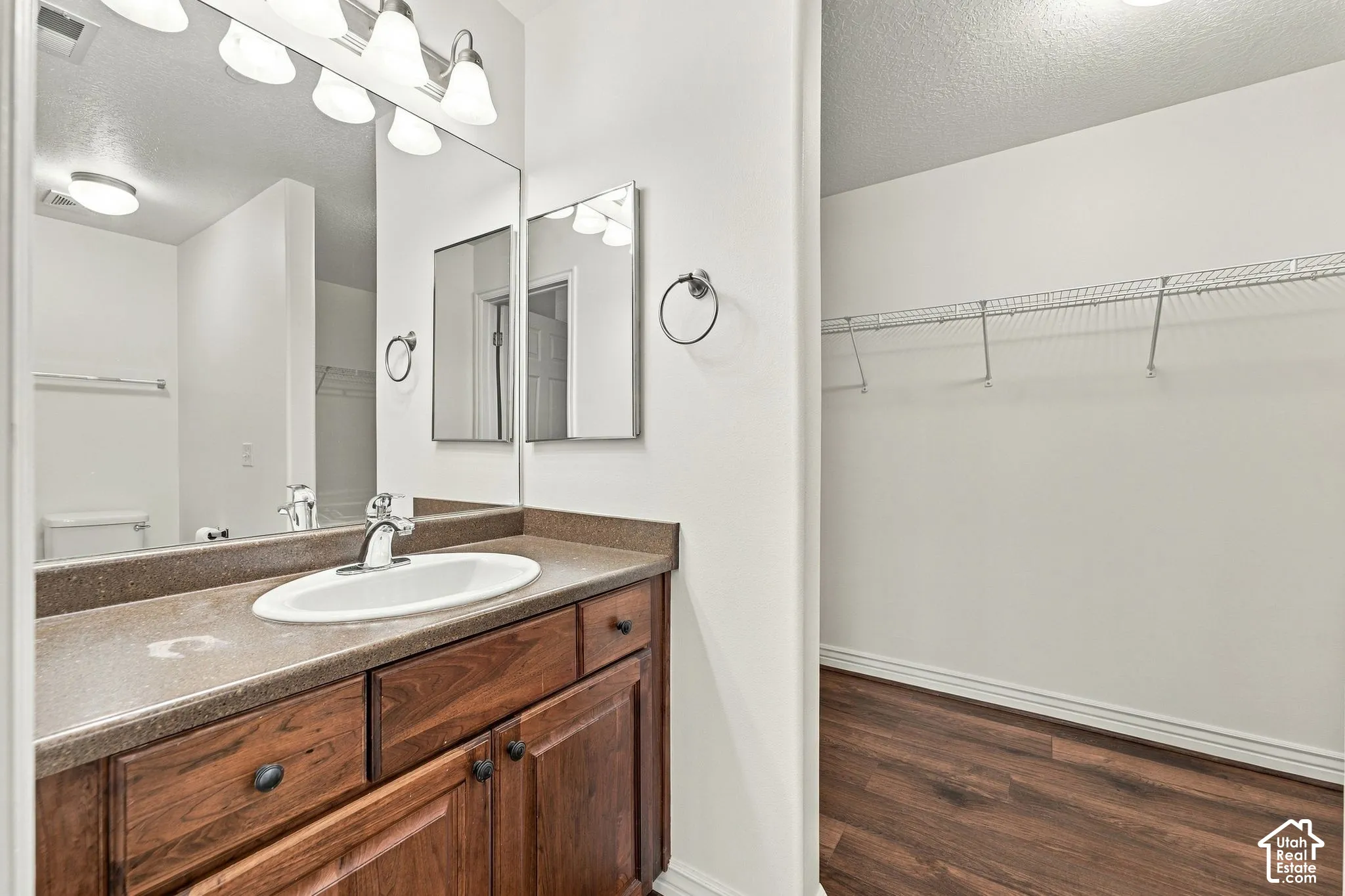 Vanity featuring a dark-finish wood cabinetry, solid-surface countertop with an integrated oval sink, full-width mirror, and attached wire shelving unit within the storage area featuring wood-finish flooring