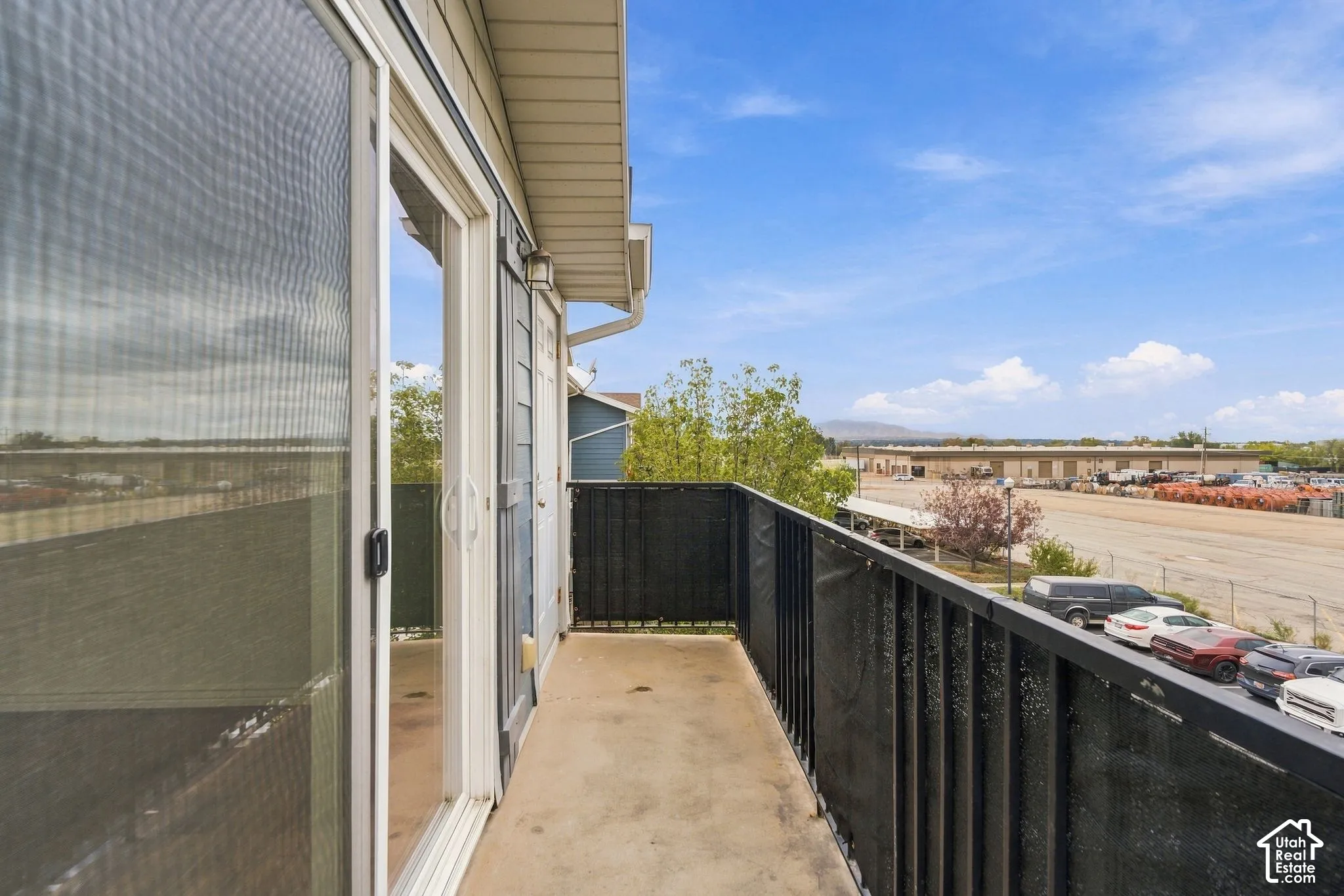 Covered balcony featuring concrete flooring, black metal railing, sliding glass door, and exterior siding