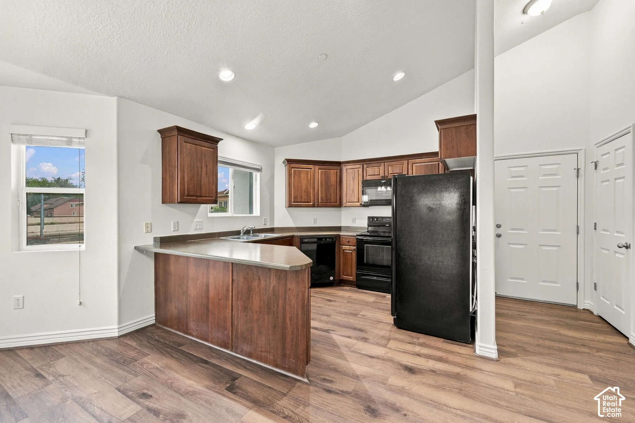 Kitchen featuring wood-finish cabinetry, hard surface countertops, wood-finish flooring, recessed lighting, and vaulted ceilings