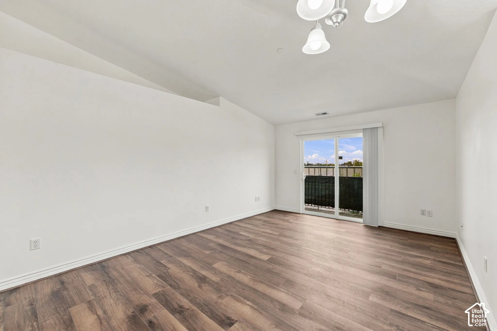 Vaulted ceiling featuring a multi-bulb pendant fixture, wood-finish flooring, and sliding glass doors with exterior access