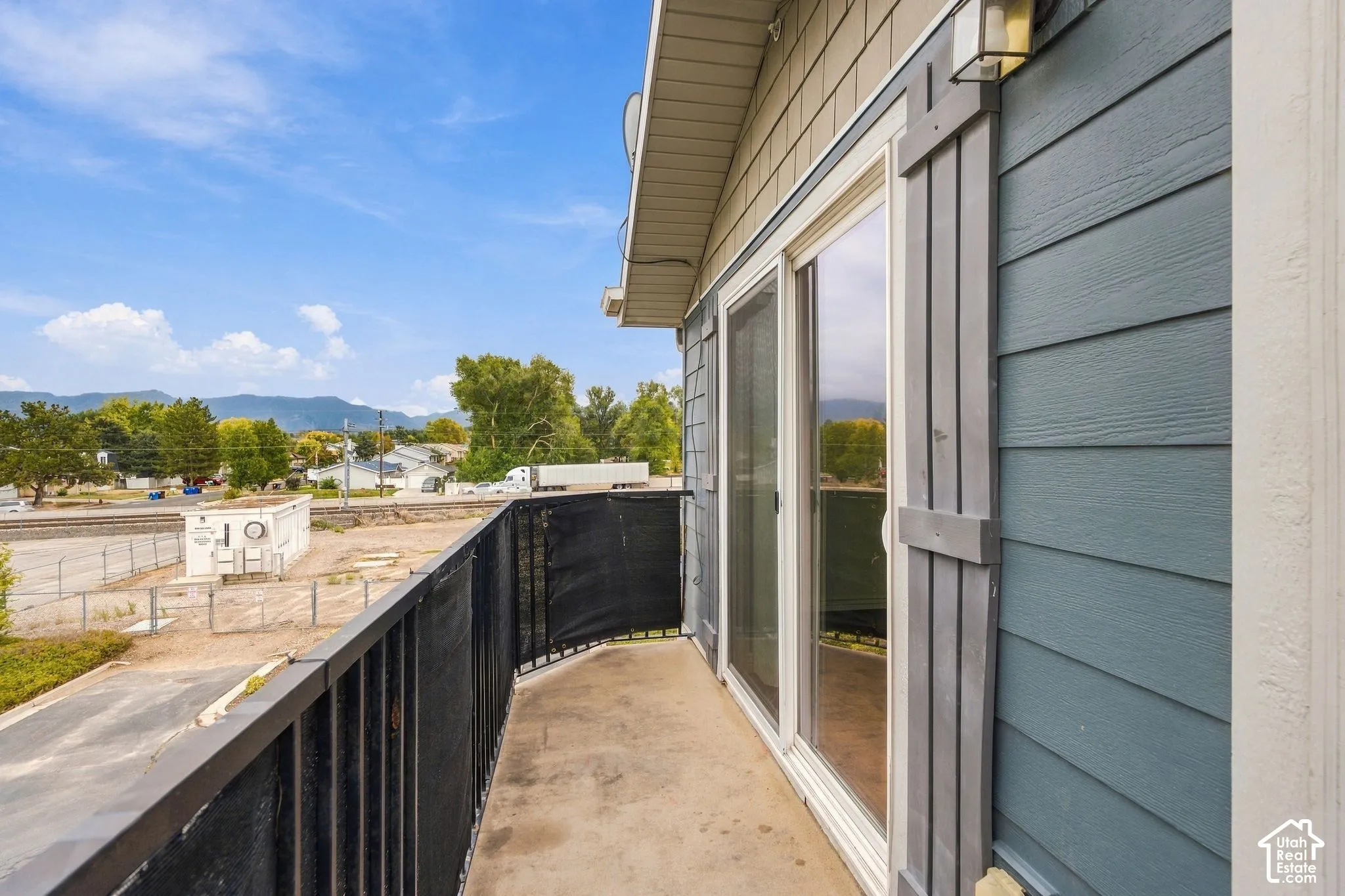 Covered balcony with black metal railing, sliding glass doors, horizontal lap siding, shingle-style gable accents, and decorative shutters