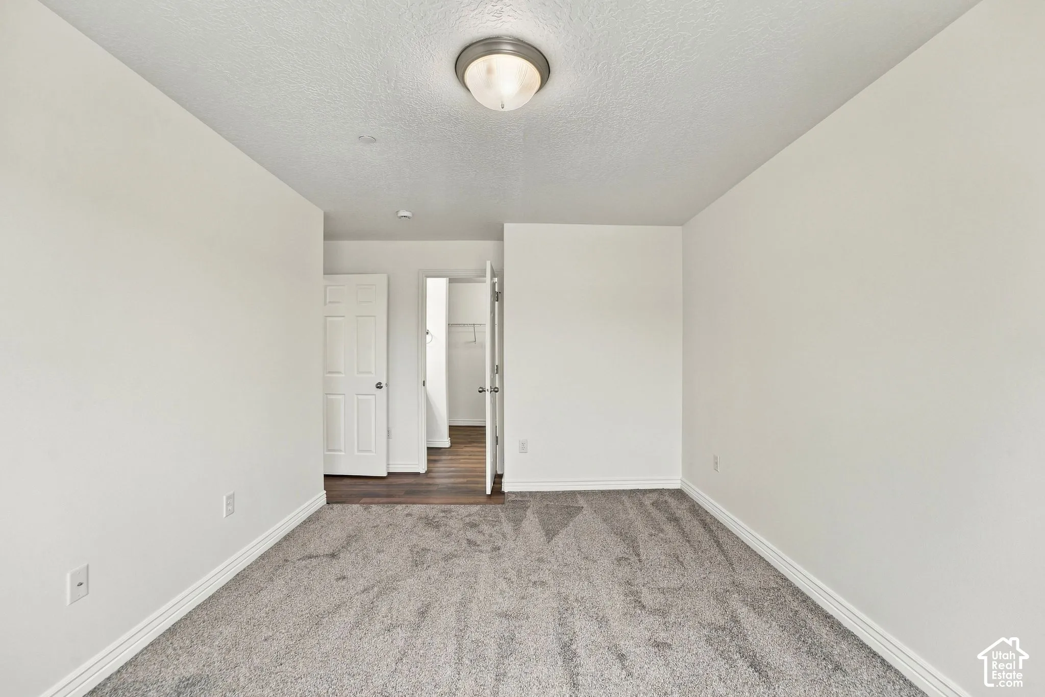Neutral-toned carpeted flooring, white interior walls, flush-mount ceiling lighting, and a six-panel door entry