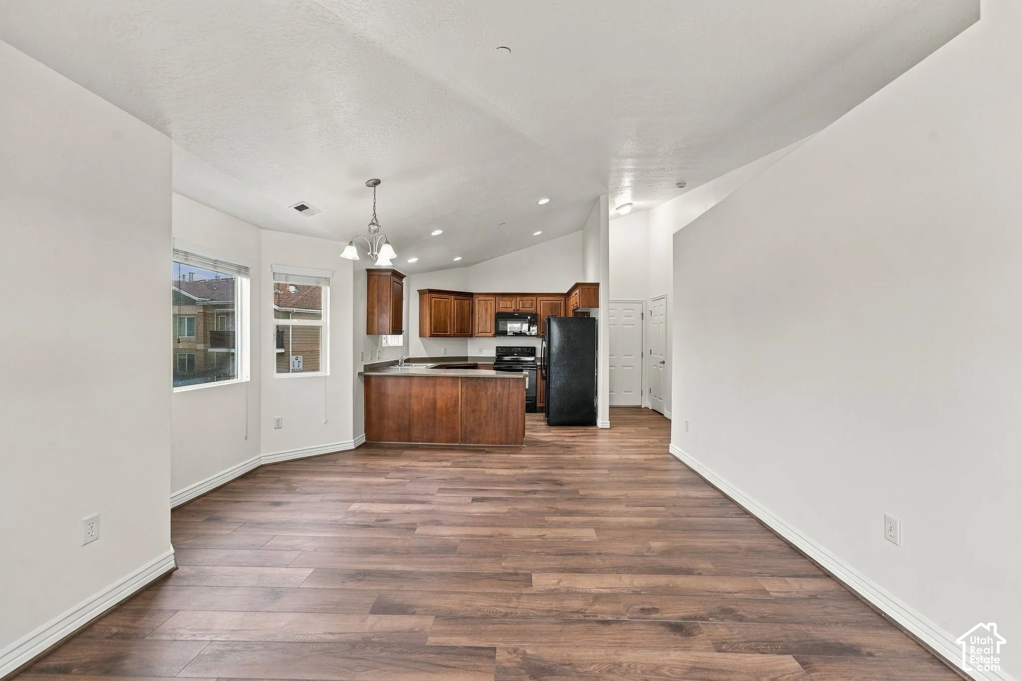 Vaulted ceilings, wood-finish flooring, recessed lighting, stained wood cabinetry, and a multi-pane pendant light fixture