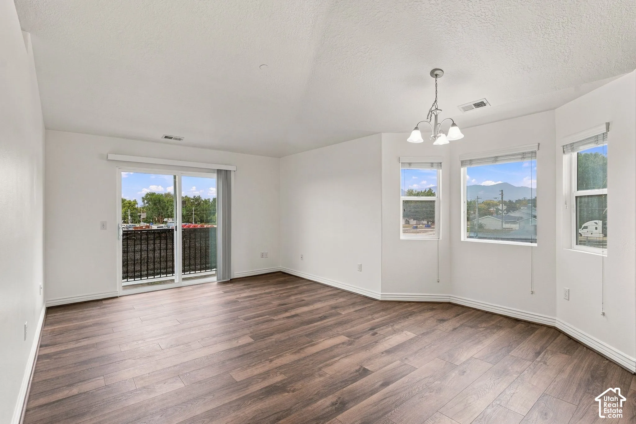 Vaulted ceilings, wood-finish flooring, bay windows, sliding glass door with balcony access, and a multi-arm chandelier