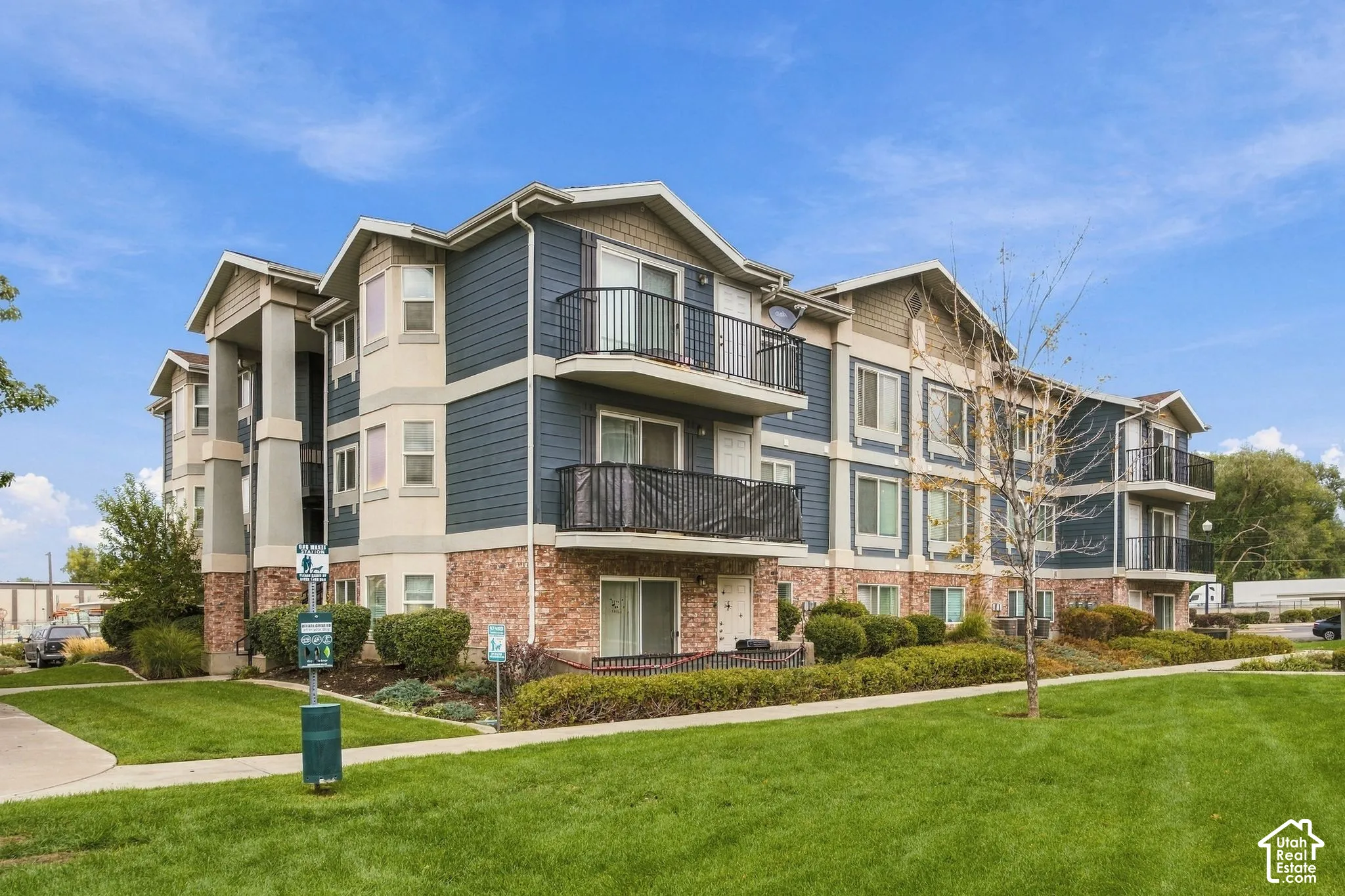 Multi-story building exterior featuring horizontal siding, brick masonry, metal balcony railings, and manicured landscaping