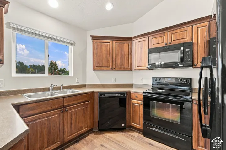 Kitchen featuring stained wood cabinetry, solid-surface countertops, dual-basin stainless steel sink, and black appliance suite