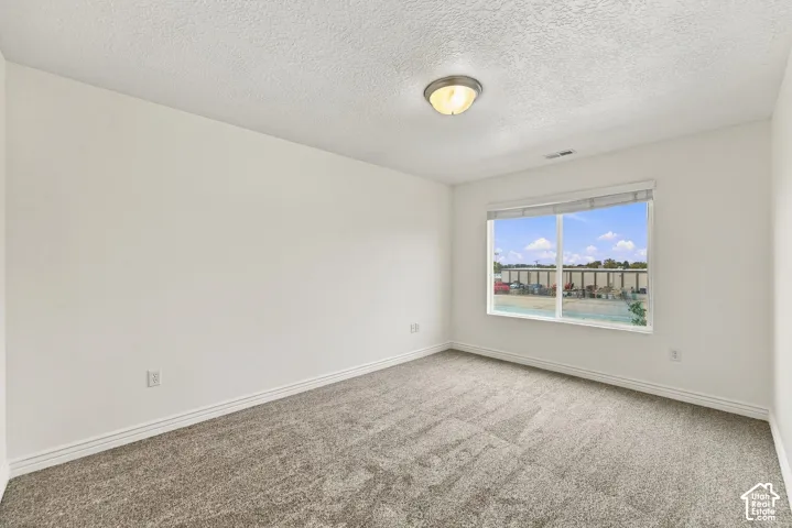 Neutral-toned wall-to-wall carpeting, crisp white walls, large picture window with adjustable blinds, and flush-mount ceiling lighting