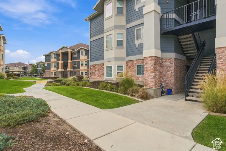 Multi-story exterior featuring blue horizontal siding, brick masonry, concrete walkways, and metal staircases