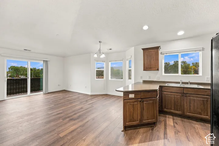 Open-concept interior featuring wood-finish flooring, dark wood-tone cabinetry, a peninsula countertop, and large windows with natural lighting
