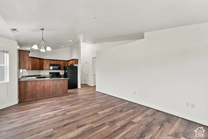 Open-concept interior featuring vaulted ceilings, wood-finish flooring, dark wood cabinetry, a breakfast bar, and recessed lighting