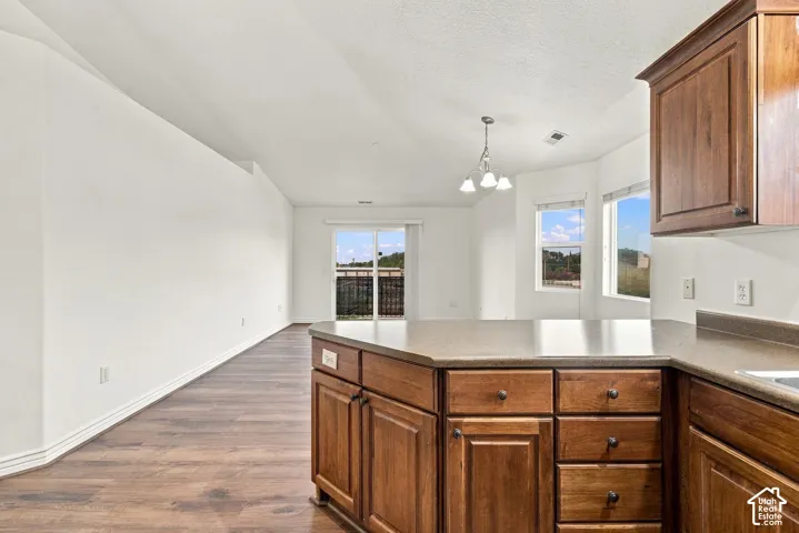 Kitchen featuring natural wood-finish cabinetry, solid-surface countertops, wood-finish flooring, vaulted ceilings, and a multi-light pendant fixture