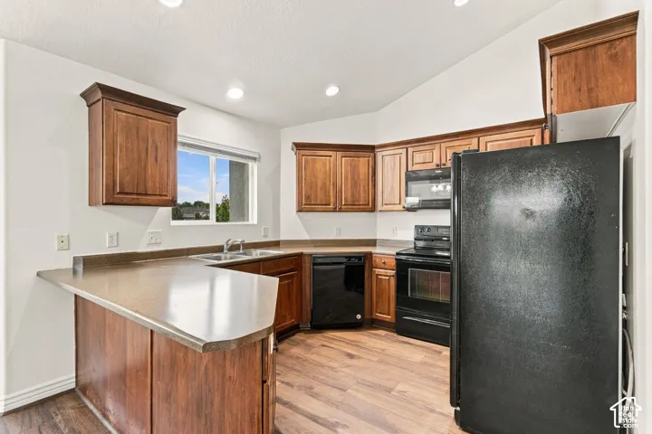 Kitchen featuring wood cabinetry, solid-surface countertops, recessed lighting, wood-finish flooring, and black appliance suite