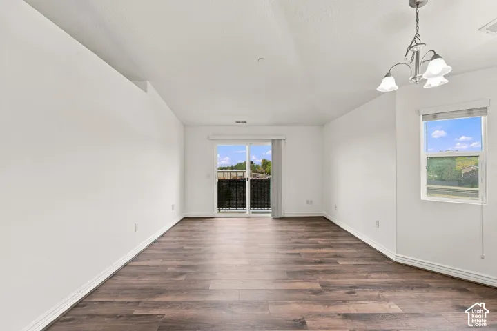 Vaulted ceiling featuring a multi-light chandelier, wood-finish flooring, and a sliding glass door providing external access