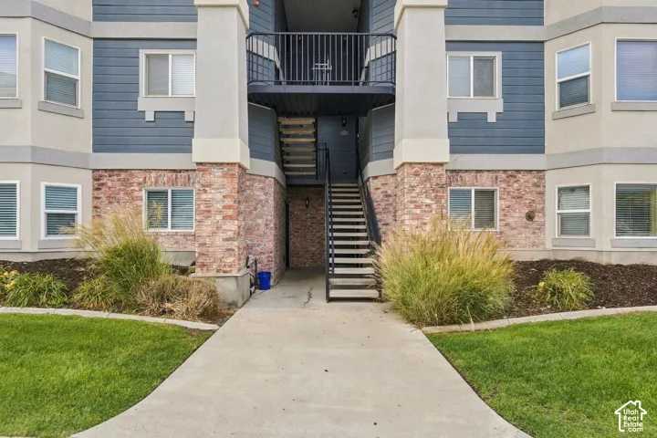 Exterior facade featuring horizontal siding, brick masonry detailing, concrete walkways, a private upper-level balcony with metal railings, and integrated stairs