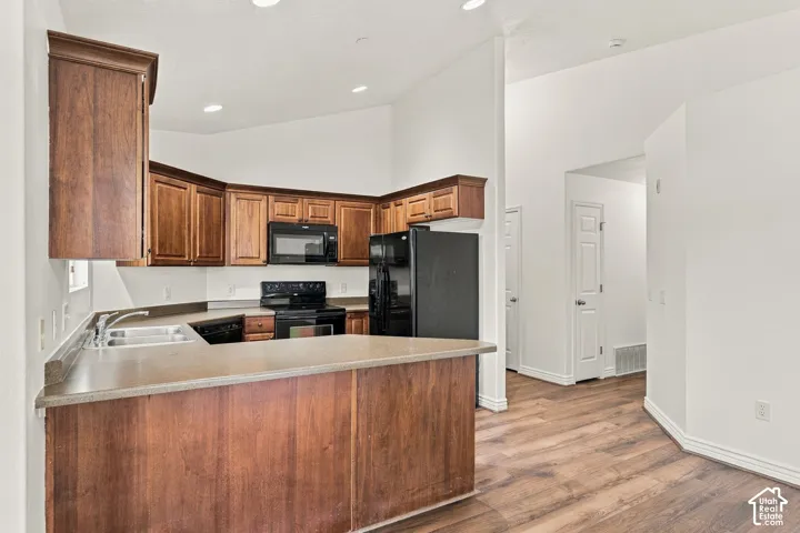 Kitchen featuring wood cabinetry, solid surface countertops, black appliances, wood-finish flooring, and vaulted ceilings