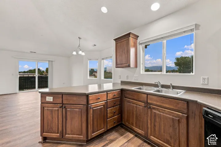 Kitchen featuring dark wood-finish cabinetry, solid-surface countertops, dual-basin stainless steel sink, wood-finish flooring, and recessed lighting