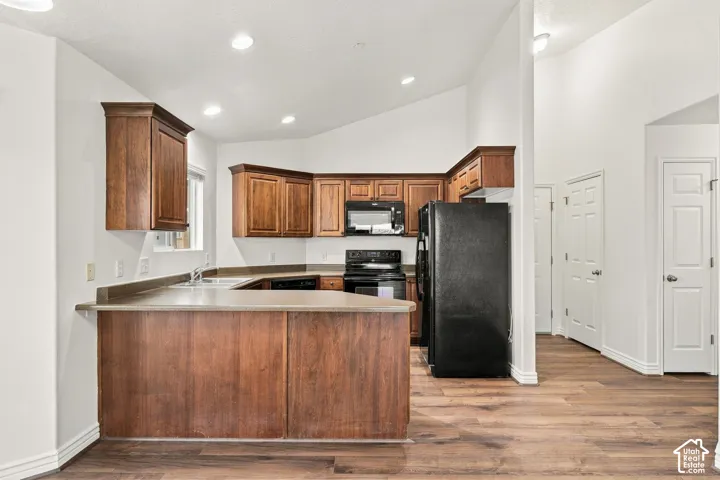 Kitchen featuring wood cabinetry, a peninsula with a solid-surface countertop, recessed lighting, and vaulted ceilings