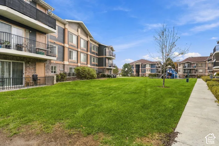 Multi-story building exterior featuring a mix of stone veneer and horizontal siding, private balconies, metal railings, and a landscaped courtyard with concrete walkways