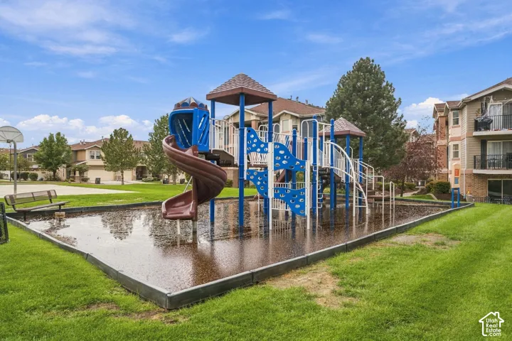 Recreational area featuring a multi-level playground structure with a spiral slide, surrounding manicured lawn, and fixed metal bench seating