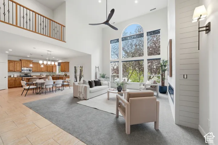 Two-story living area featuring vaulted ceilings, floor-to-ceiling windows, a horizontal plank fireplace surround, iron spindle railing, and a minimalist ceiling fan