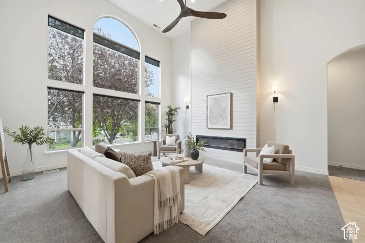Floor-to-ceiling windows featuring an arched design, shiplap-style fireplace surround, linear electric fireplace, and a contemporary ceiling fan