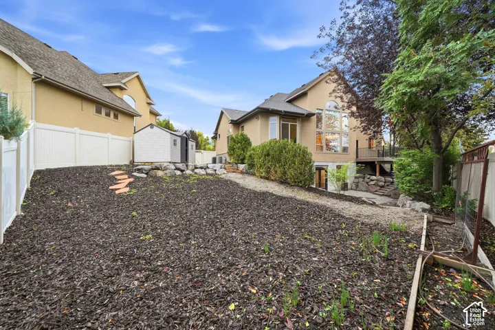 Backyard featuring multi-level landscaping with mulch beds, stone retaining walls, white vinyl privacy fencing, and a detached storage shed