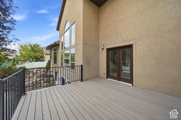 Composite decking with a black metal railing, stucco exterior, multi-pane floor-to-ceiling windows, and French door access