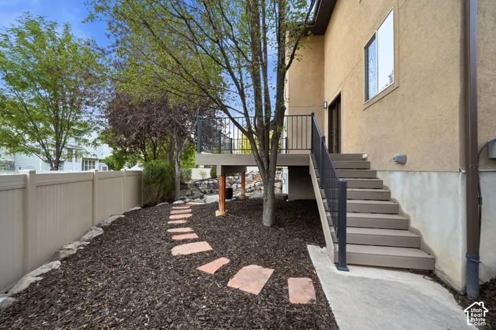 Elevated deck featuring black metal railing, stairs with coordinating handrail, stone-finish path, and privacy fencing