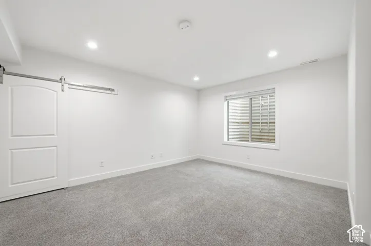 Neutral-toned carpeting, recessed ceiling lighting, and a white sliding barn door featuring matte hardware, complemented by a window with a window well