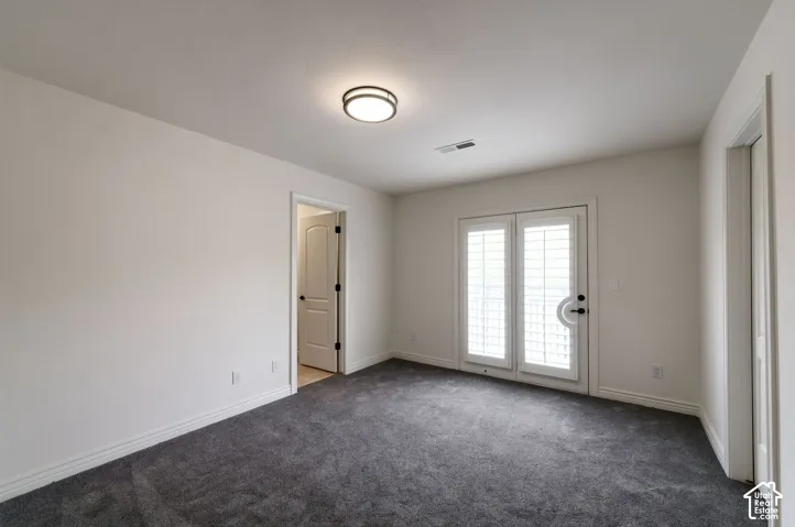 Interior room featuring neutral wall paint, wall-to-wall carpeting, flush-mount lighting, and dual glass-paneled doors with interior plantation shutters