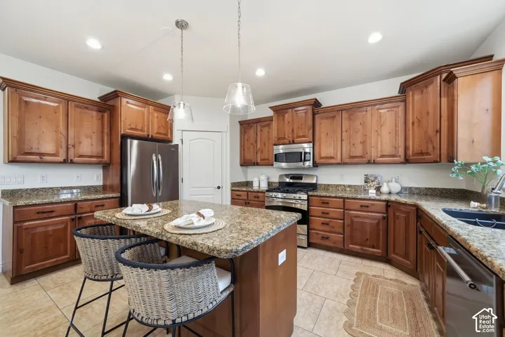 Kitchen featuring knotty wood cabinetry, stone-surface countertops, central island, stainless steel appliances, and tile flooring
